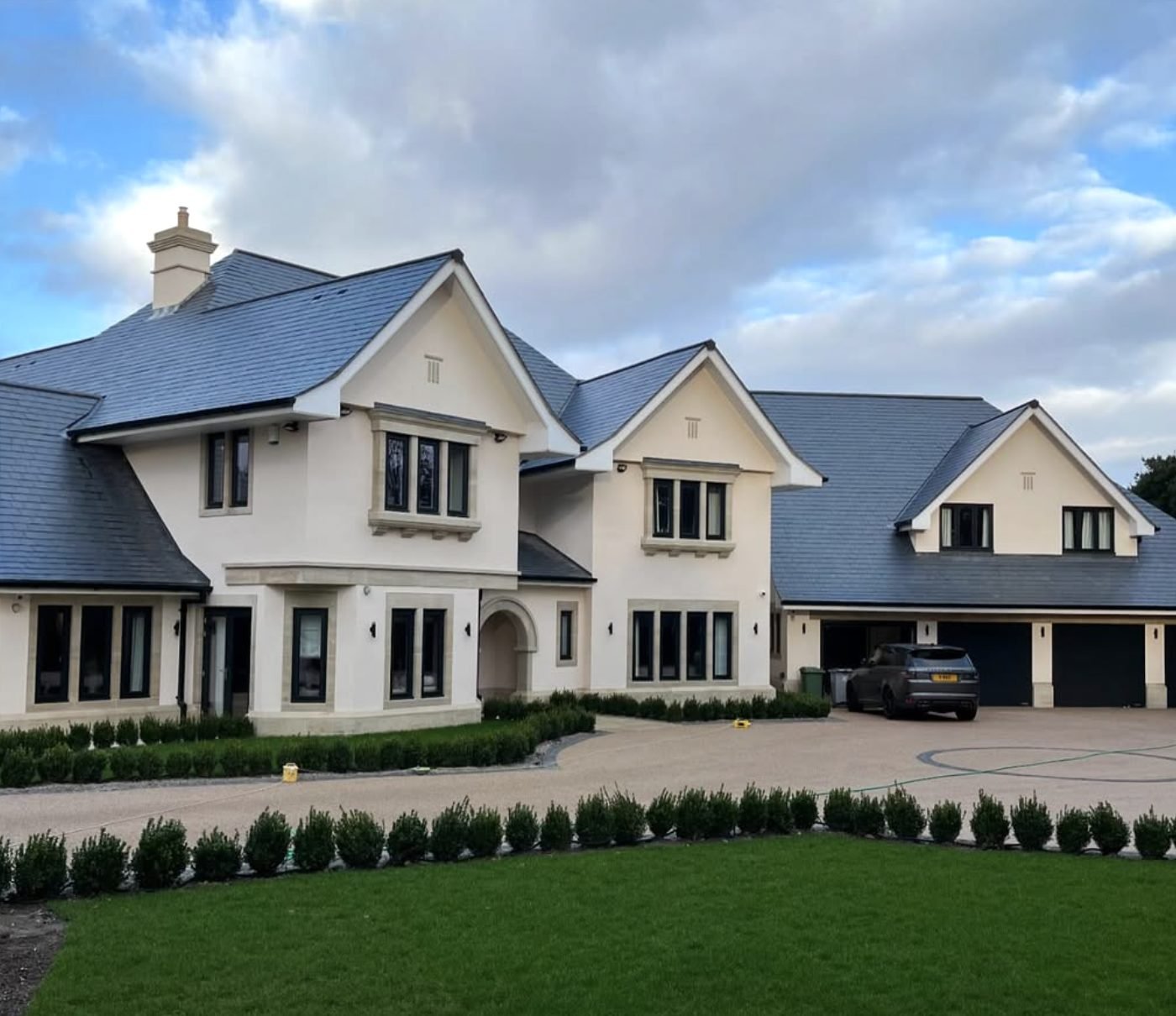 Large detached house in cream render behind a gravel drive