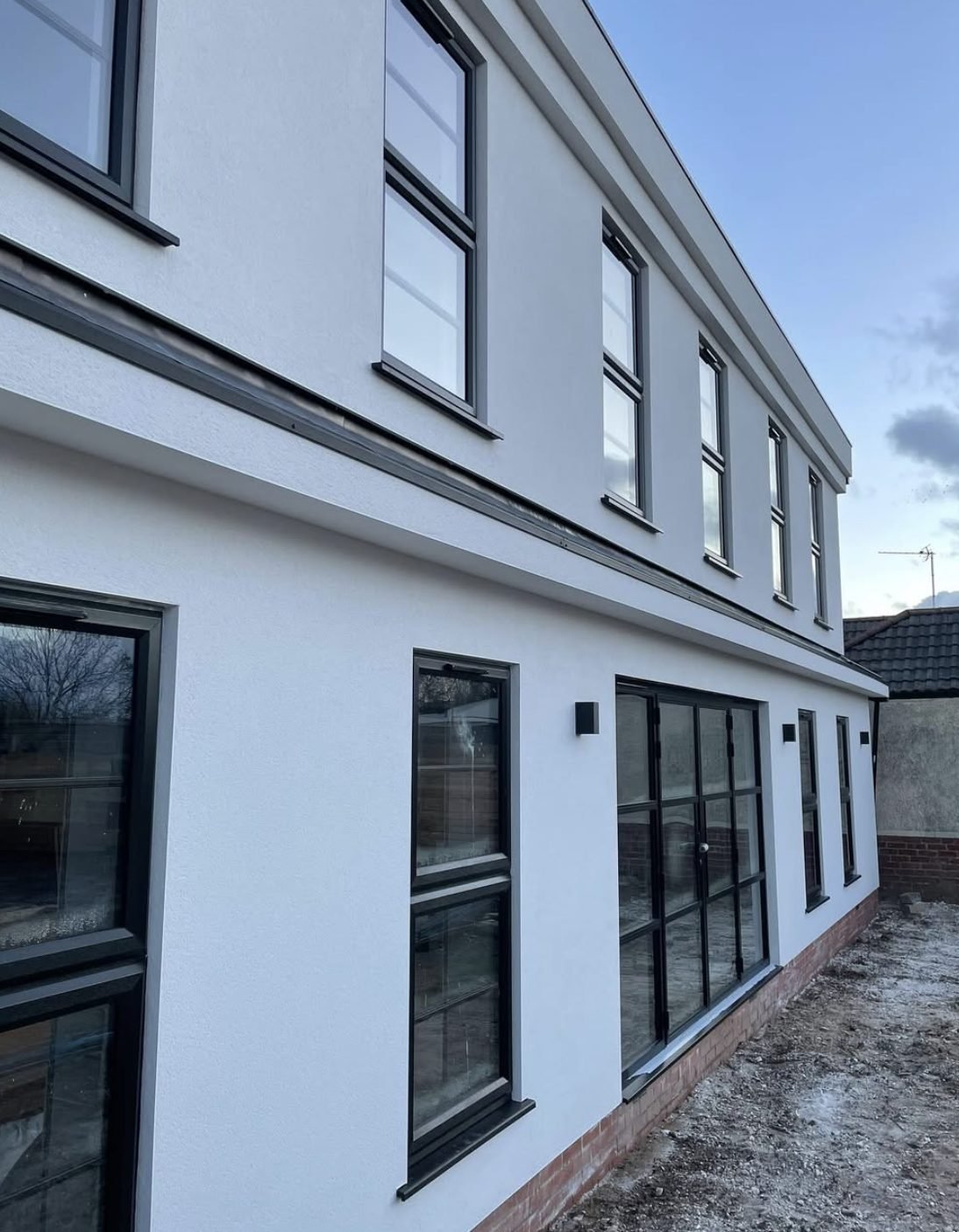 Long two-storey side wall in white render with black windows and a dark band