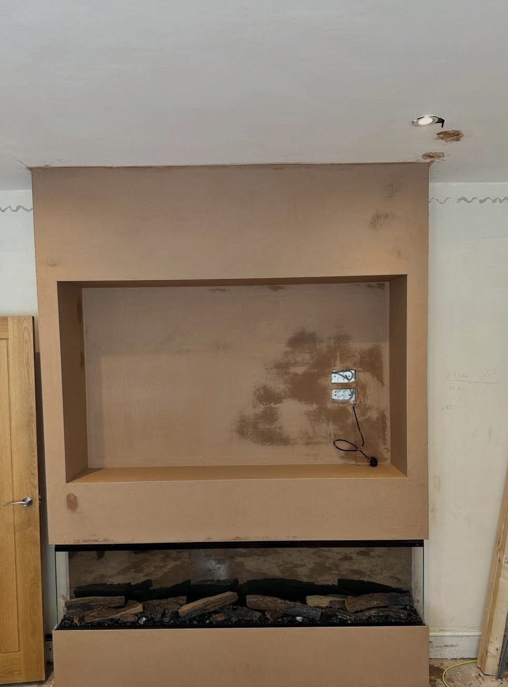 Freshly plastered media wall with a recess for a television and a fire opening below
