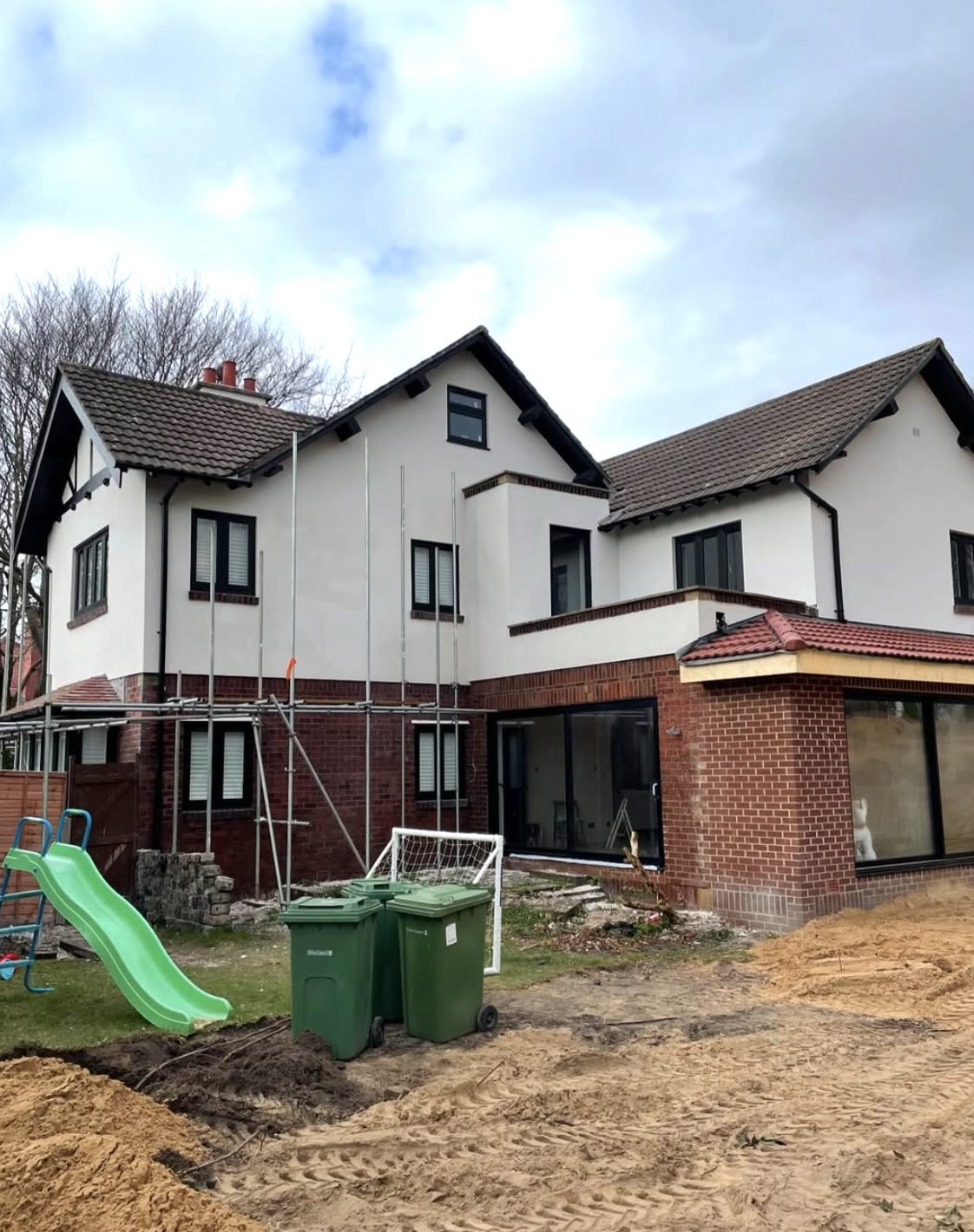 Back of a large house with the upper floor rendered and scaffold around a brick extension