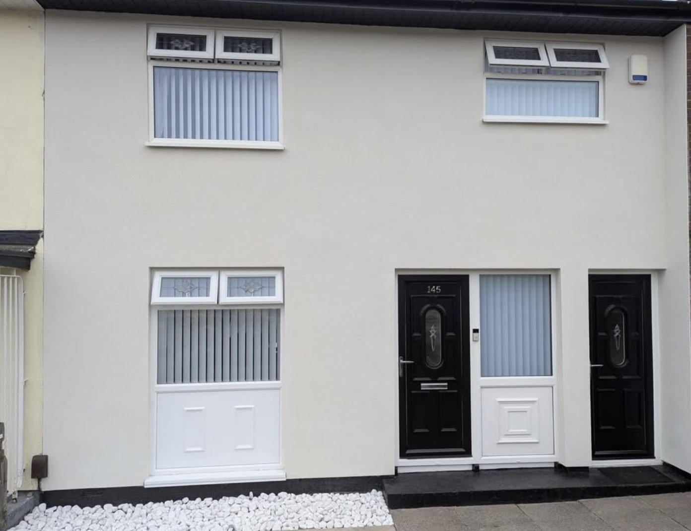 Flat-fronted terraced houses in smooth cream render with black front doors